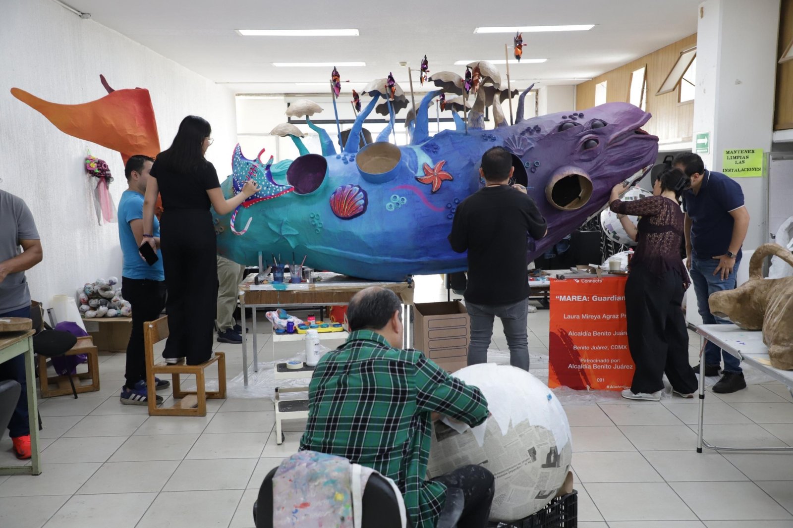 Equipo artístico pinta un alebrije marino azul y violeta llamado Marea Guardiana BJ para el Desfile de Alebrijes 2026 en la Ciudad de México