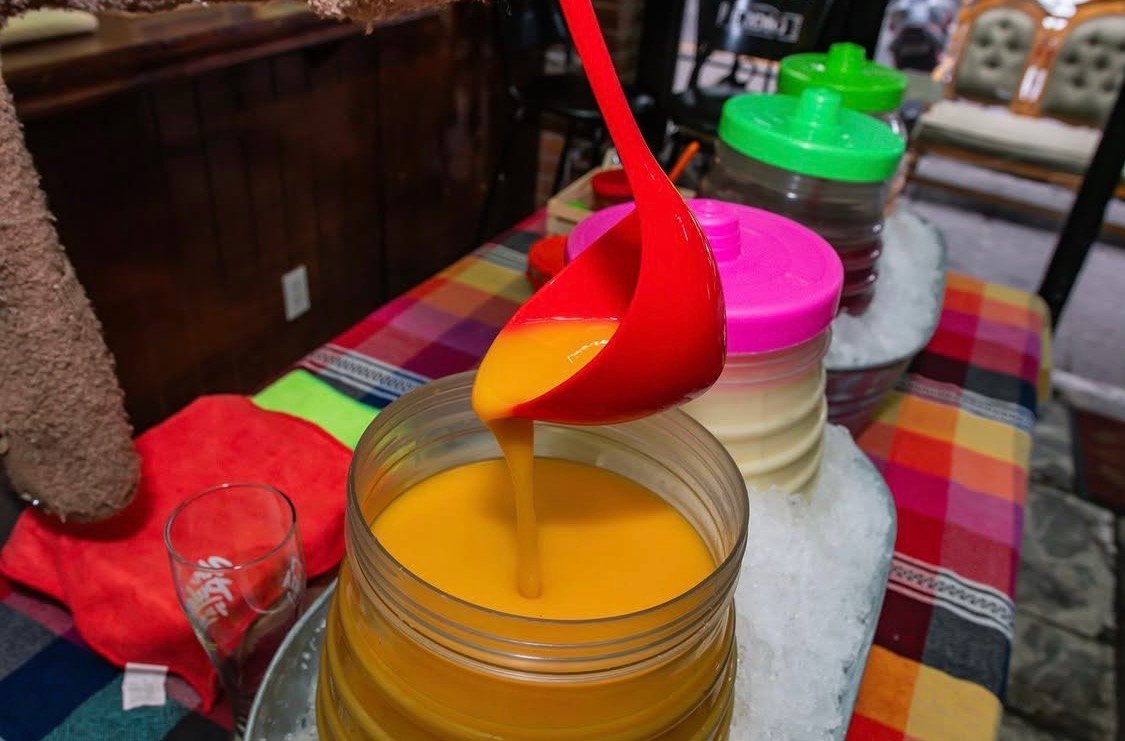 Cucharón rojo con bebida anaranjada sobre recipiente en la barra de Cantina Masiosare