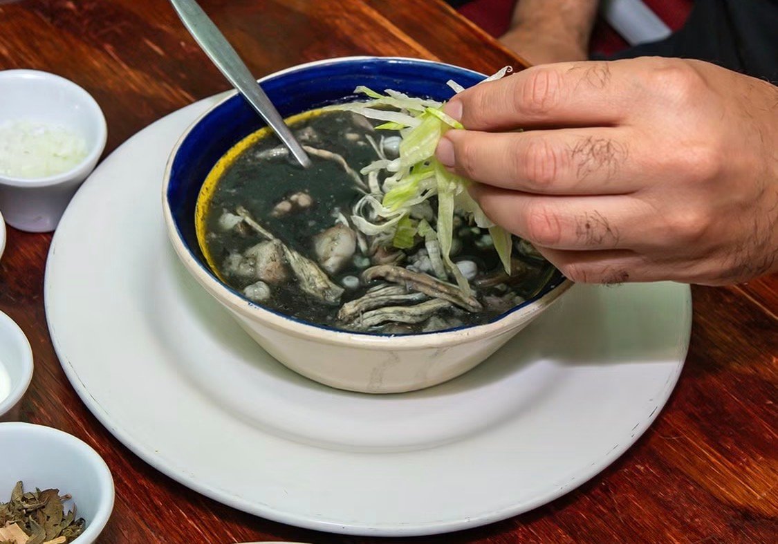 Plato de caldo oscuro con carne y vegetales frescos servido en Cantina Masiosare